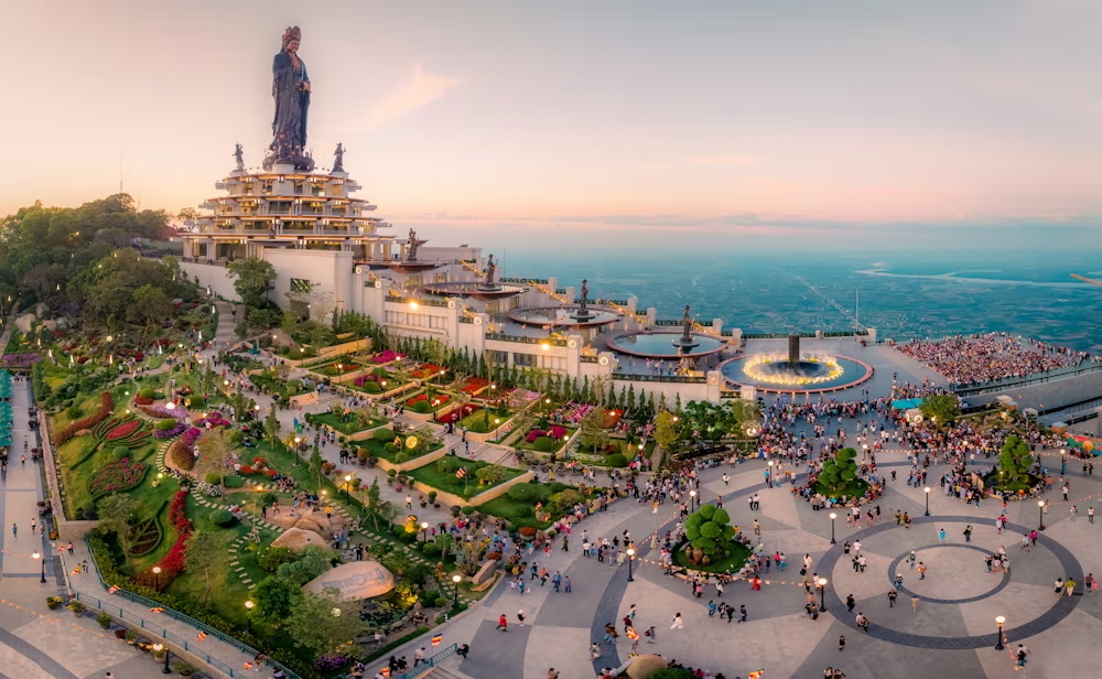 The towering Tay Bo Da Son Buddha statue overlooking crowds and a vibrant mountain landscape