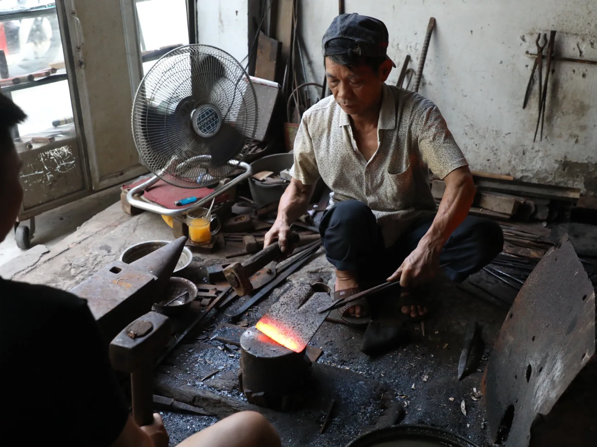 Người thợ rèn là đứng bên lò lửa đỏ rực, sử dụng bễ thổi và các công cụ thủ công để rèn sắt
