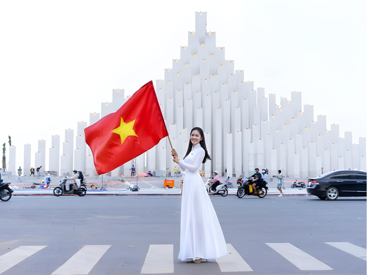Du khách check-in tại Tháp Tam Thắng cùng bộ áo dài trắng và cờ đỏ sao vàng.